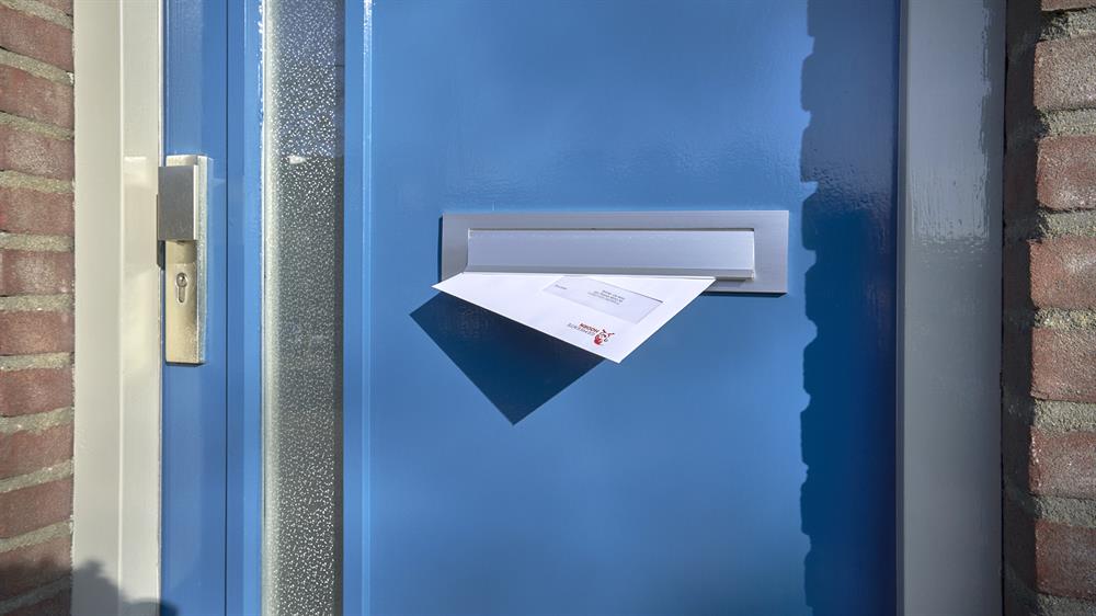 Een blauwe voordeur waar een brief van de gemeente Hoorn uit de brievenbus steekt