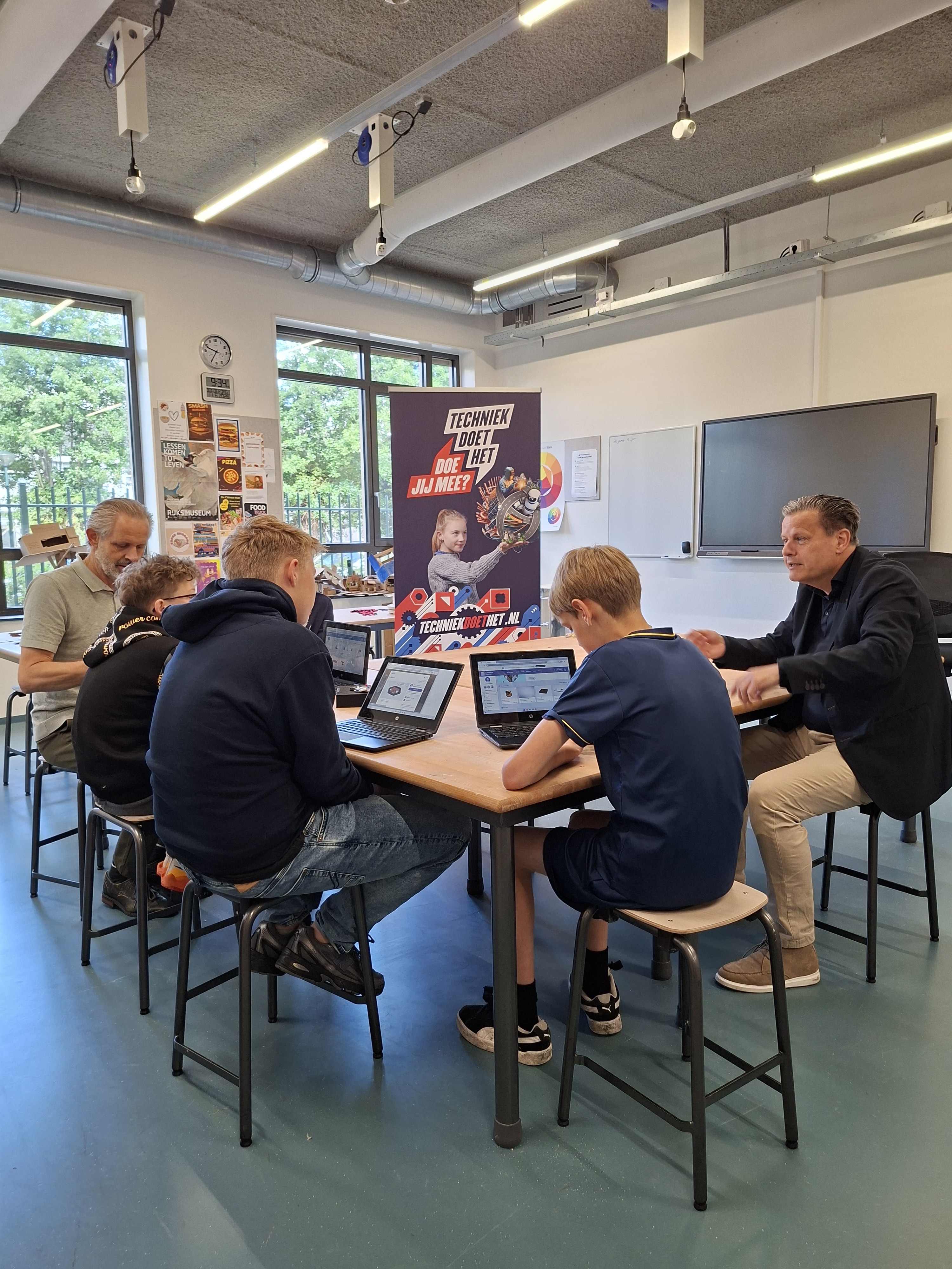 Een docent, leerlingen en wethouder Assendelft in het klaslokaal